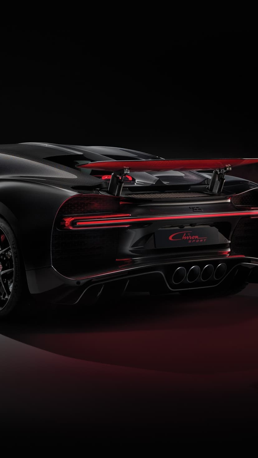Rear of a black Bugatti Chiron Sport with red LED tail light bar and quad exhausts on a dark background.