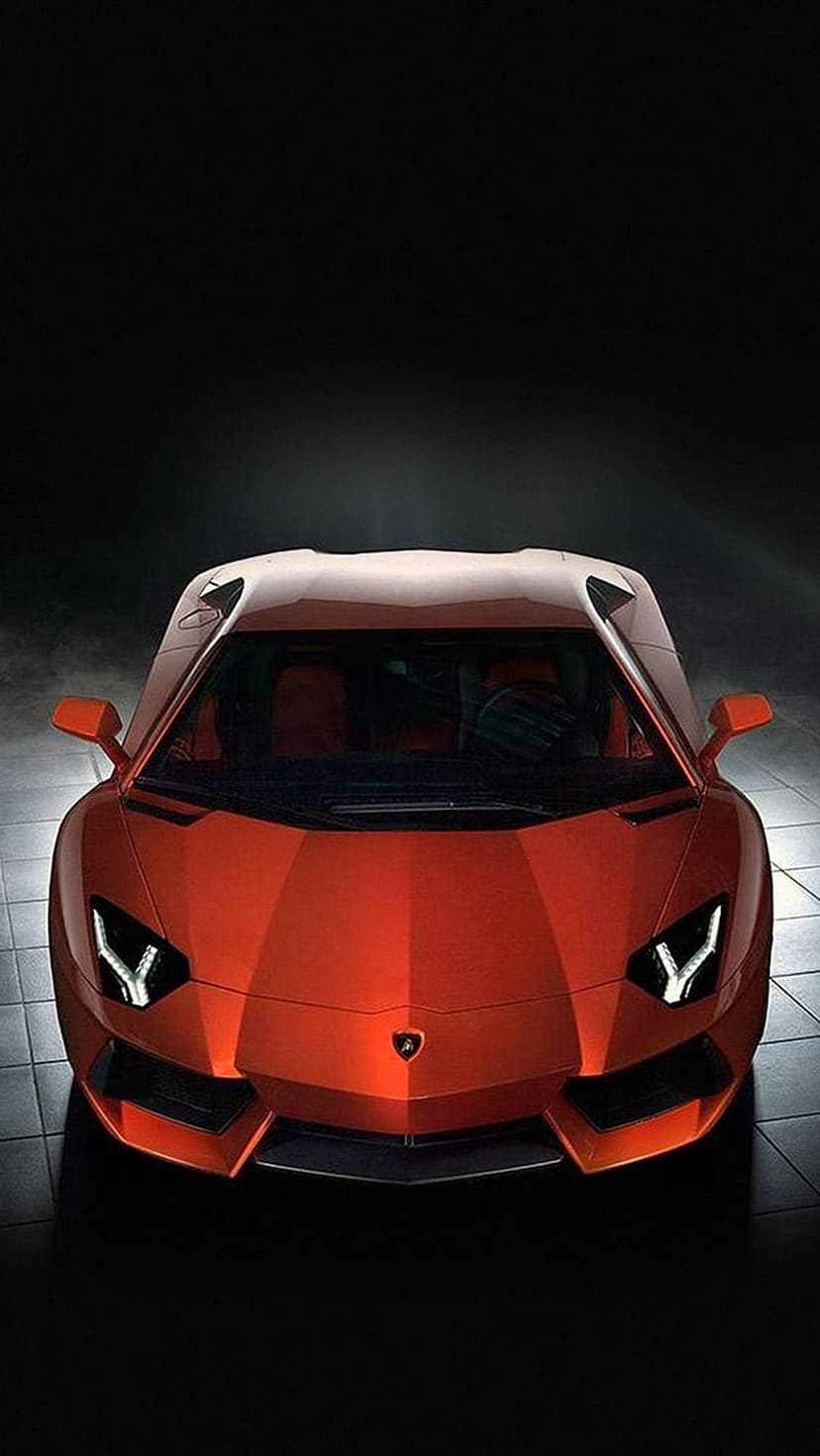 Orange Lamborghini Aventador featuring sharp aerodynamic lines and glowing headlights against a dark background.