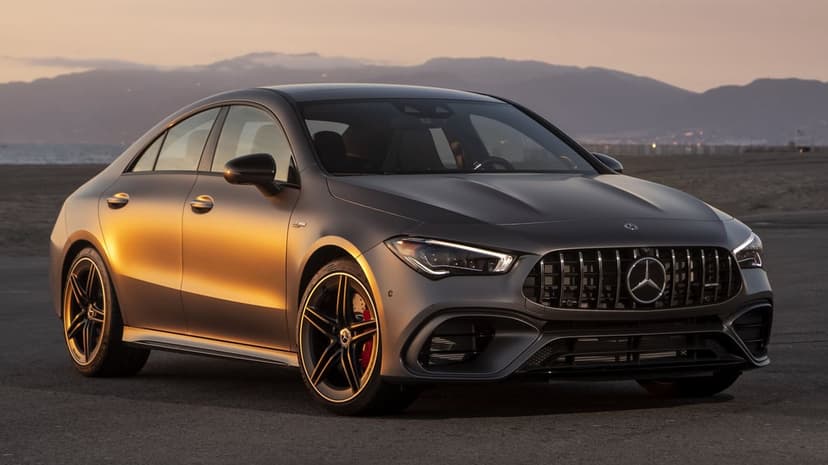 Matte grey Mercedes-AMG sports sedan at sunset with golden reflections on its side and distant mountains.