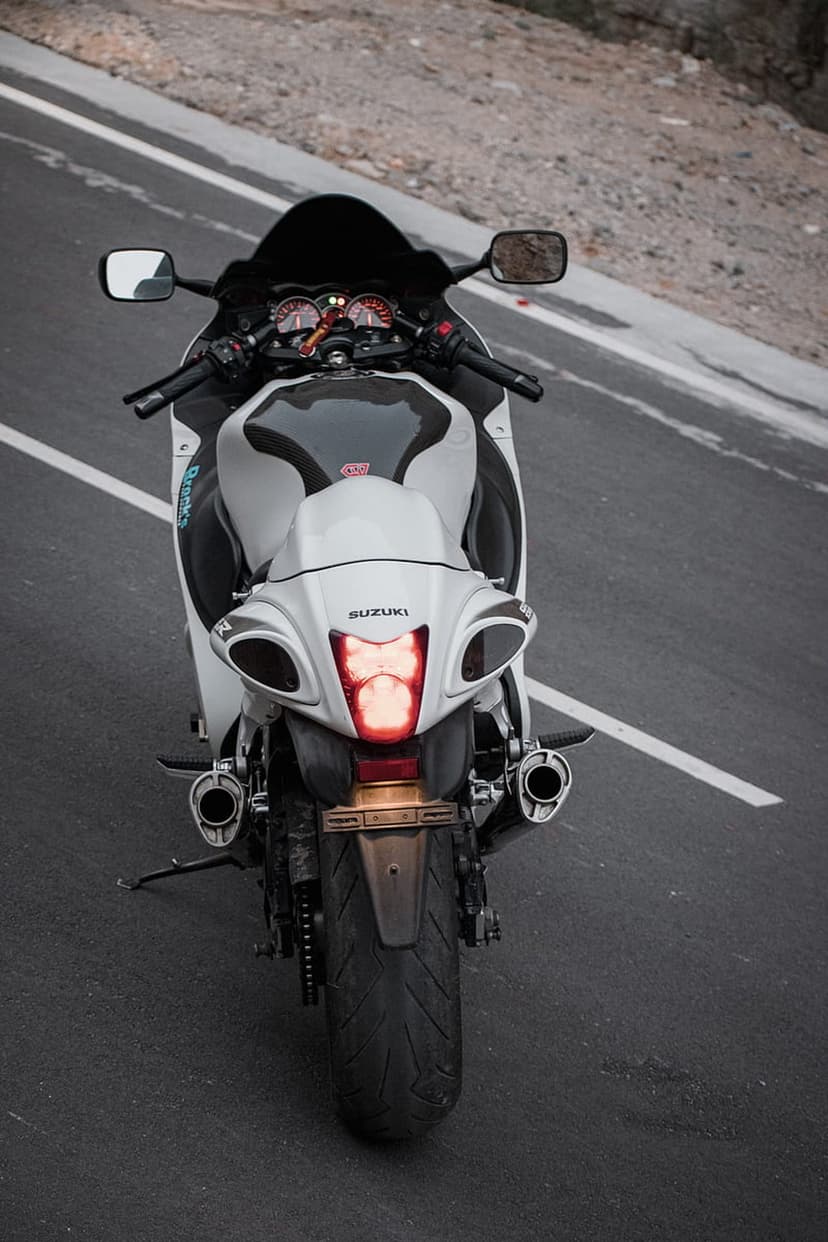 Suzuki Hayabusa motorcycle rear view with illuminated red tail lights parked on a winding road during twilight.