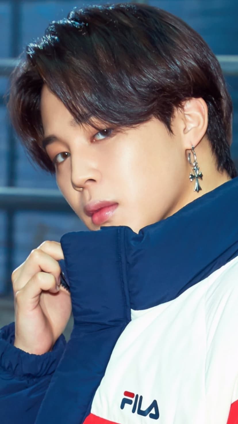 Jimin of BTS wearing a black Fila jacket and silver earring while holding his collar in a close-up portrait.
