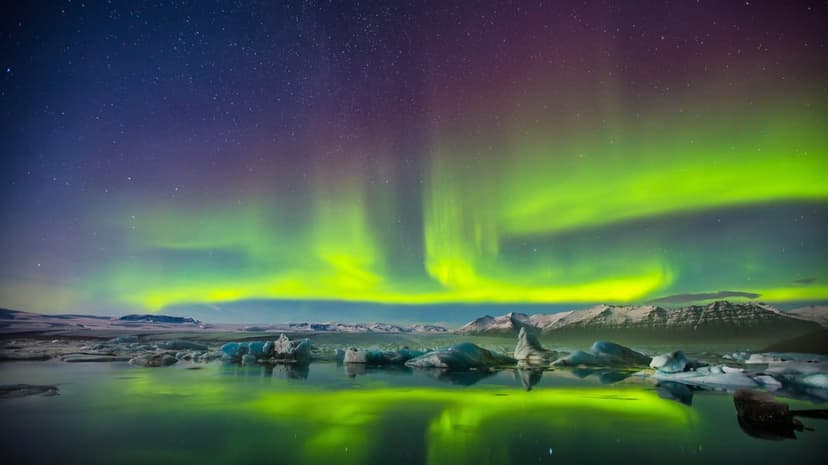 Northern lights display green ribbons over a white snow field under a dark night sky with visible stars.