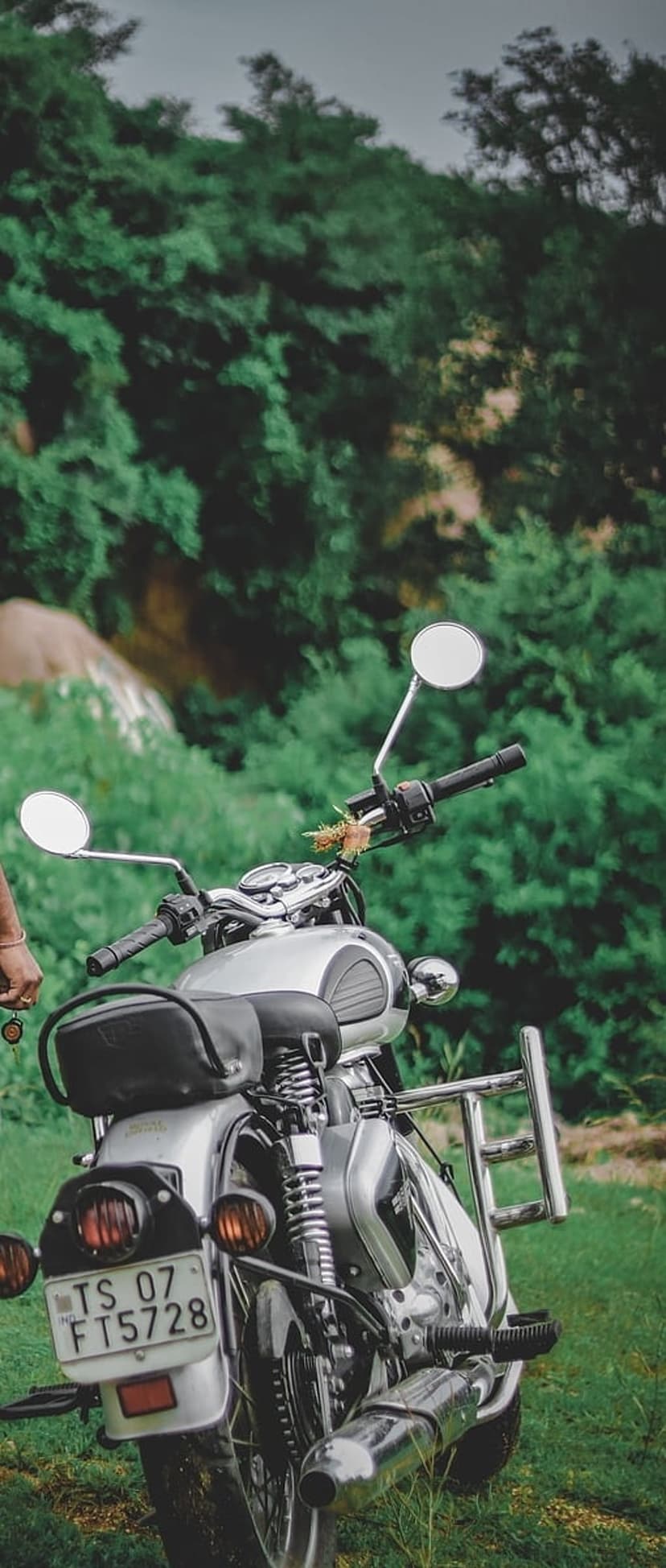 Silver Royal Enfield motorcycle with chrome accents parked in a dense green forest with soft natural lighting.