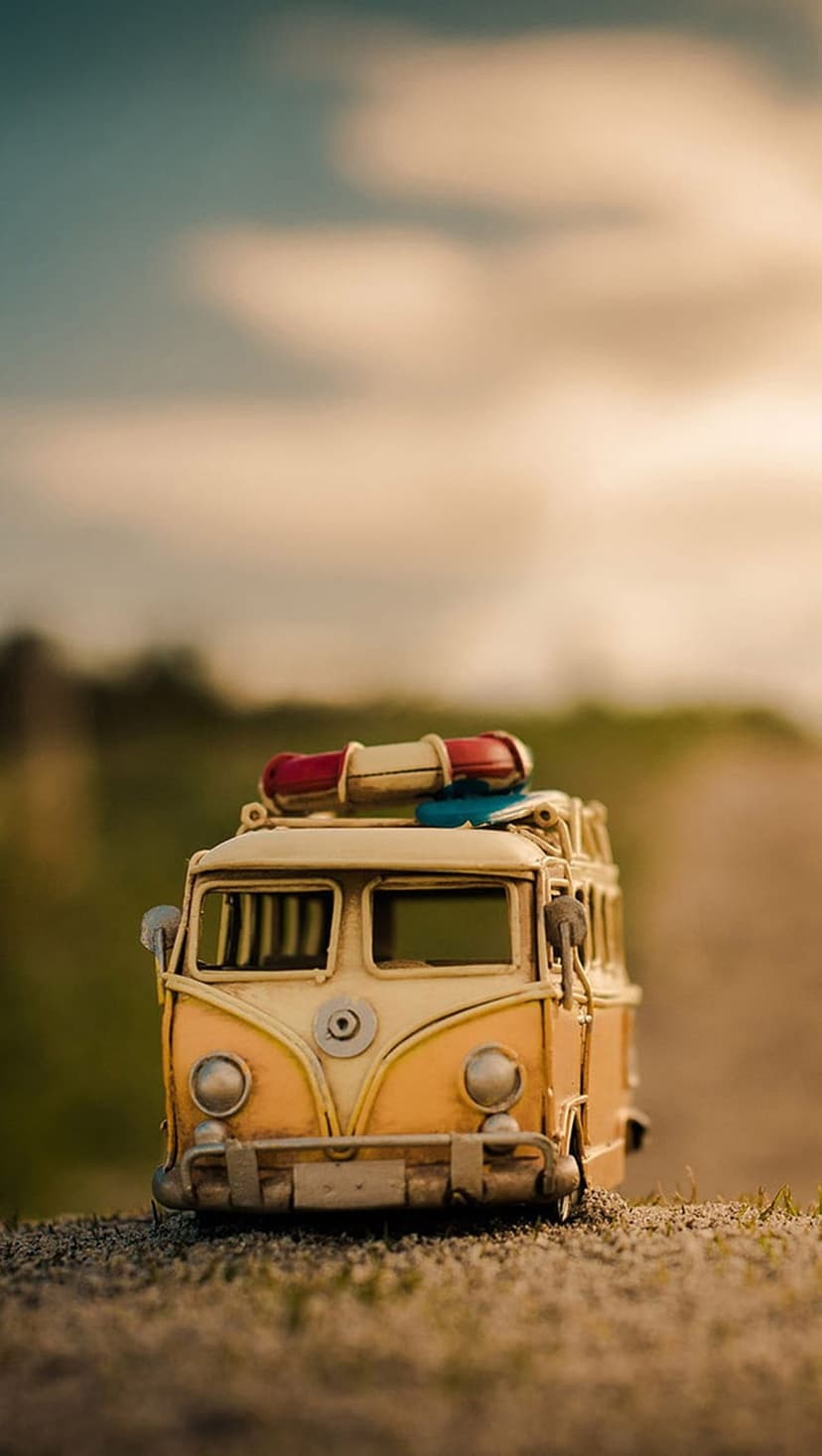 Miniature yellow camper van with luggage on its roof sits on a gravel path with a blurred background.