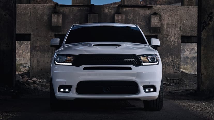 Front view of a white Dodge Durango SRT with glowing headlights in a dark industrial concrete setting.