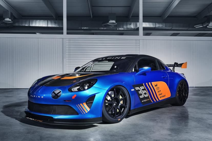 Blue Alpine A110 GT4 race car with orange livery parked in a modern industrial garage with bright lighting.