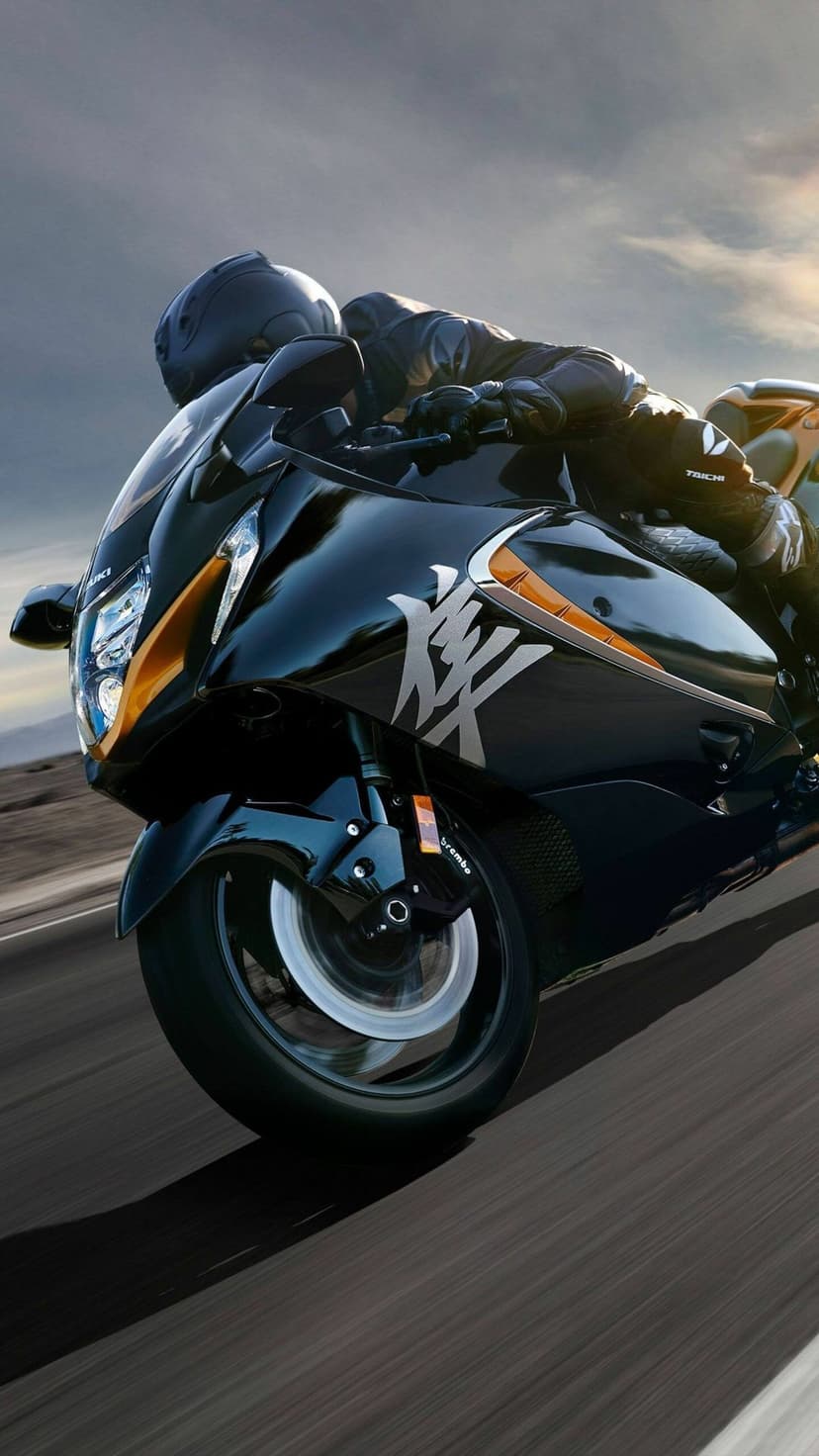 Black Suzuki Hayabusa motorcycle leans into a turn at high speed with motion blur on a dark asphalt road.