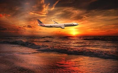 Airplane Flying Over Ocean at Sunset