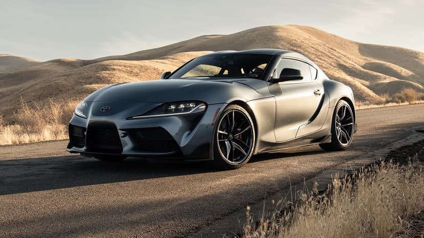 Silver Toyota Supra A90 parked on a winding road with rolling dry hills and warm golden hour lighting.