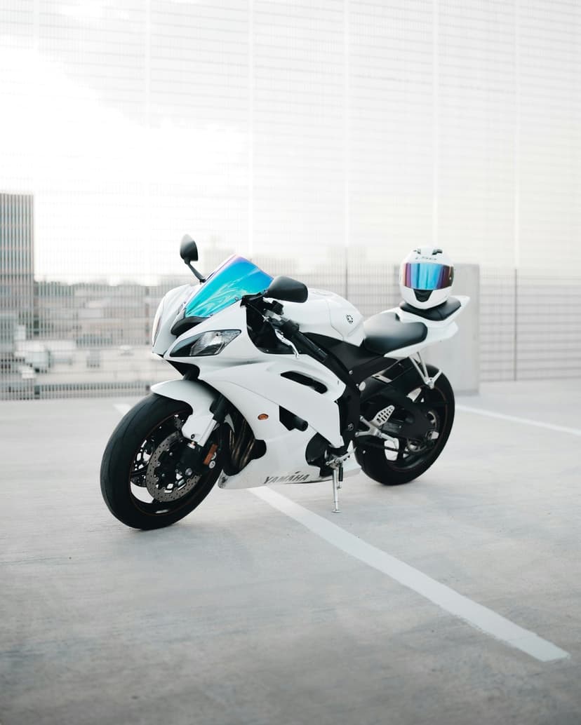 White Yamaha motorcycle with a blue windshield and matching helmet parked against a blurred city skyline backdrop.