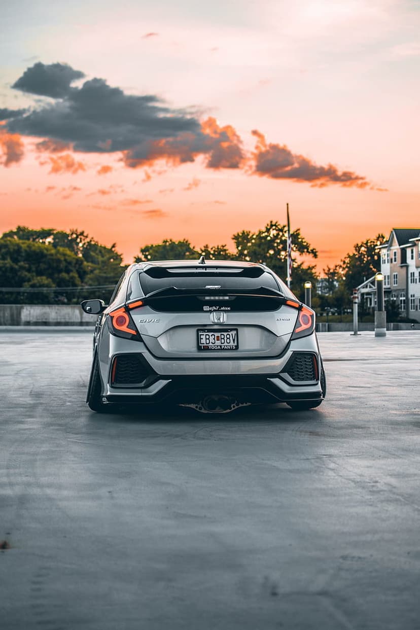 Silver Honda Civic hatchback with modified taillights parked on concrete under an orange and pink sunset sky.