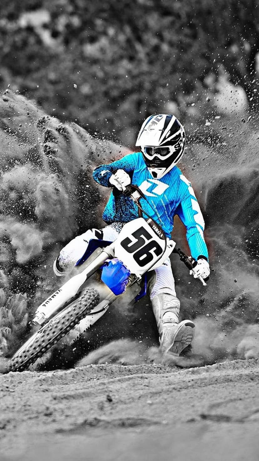 Motocross rider in a blue suit leans into a turn as thick dust and dirt erupt around the motorcycle wheels.