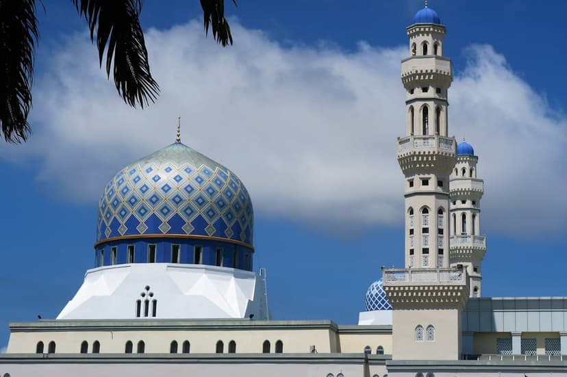 Kota Kinabalu City Mosque featuring a blue patterned dome and white minarets against a clear sky with clouds.