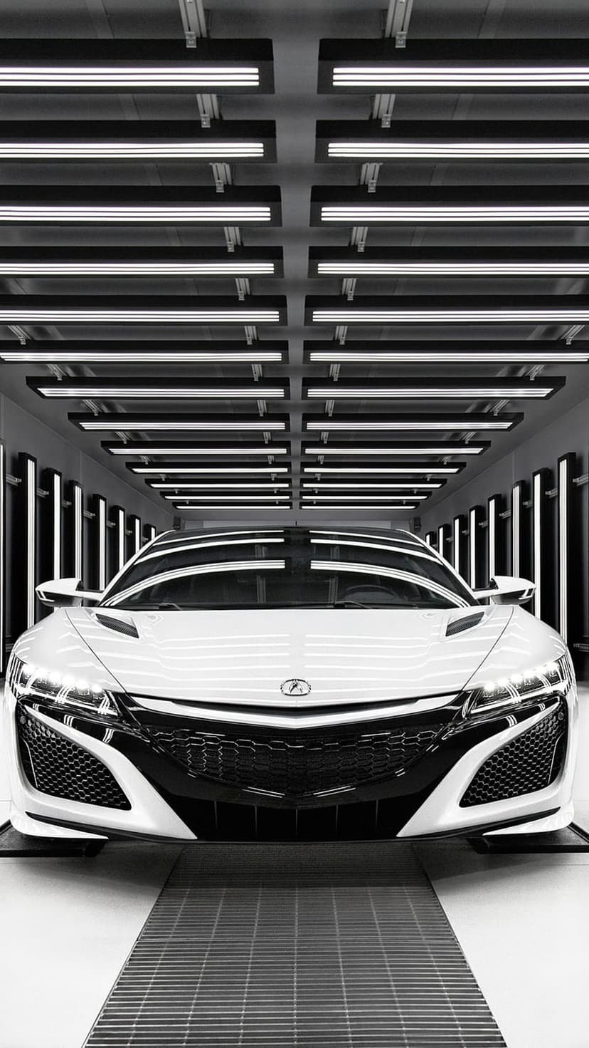 White Acura NSX sports car parked under linear ceiling lights in a dark, contemporary automotive studio.