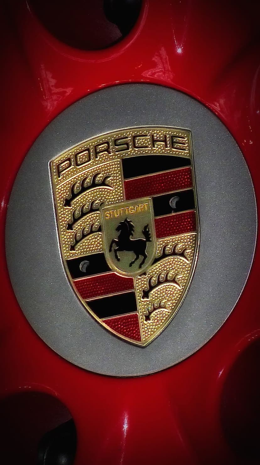 Porsche gold crest with the Stuttgart horse sits on a vibrant red reflective car body in close-up detail.