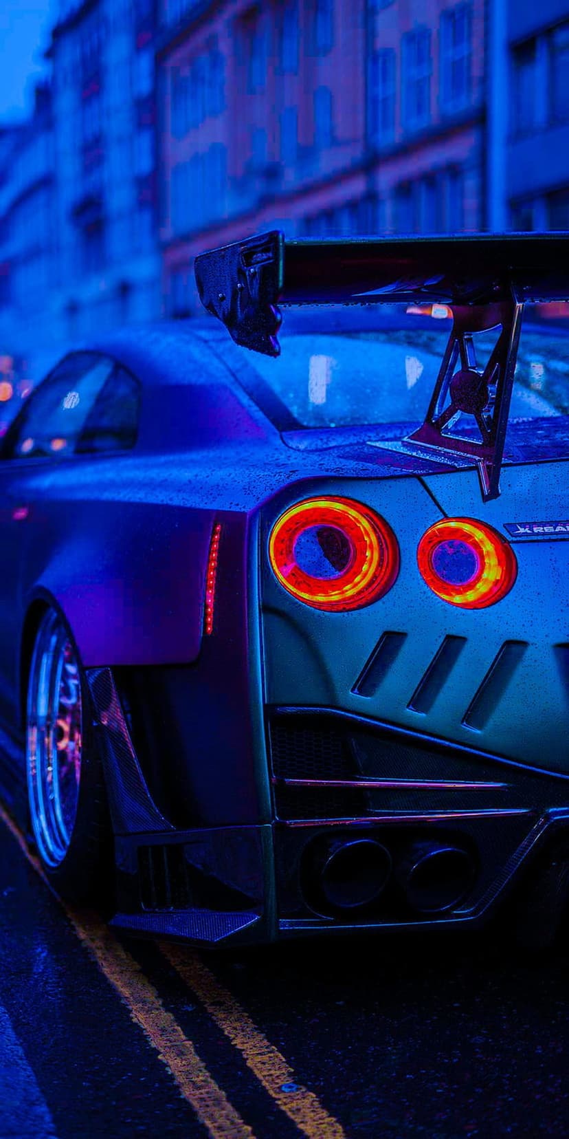 Nissan GT-R rear view with a large wing and glowing circular taillights on a wet, neon-lit midnight street.