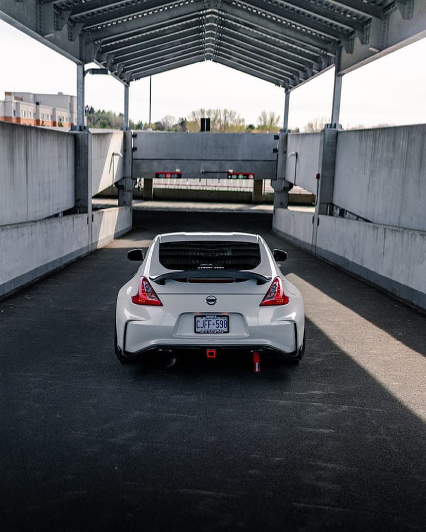 Nissan 370Z rear bumper with red tow hooks and spoiler in a concrete underpass with dramatic sunlit shadows.
