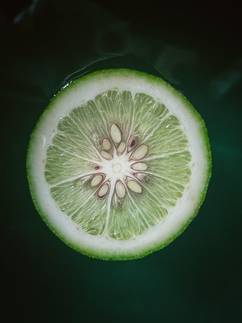 Lime slice with translucent green segments and seeds floating in deep emerald water shown from an overhead view.