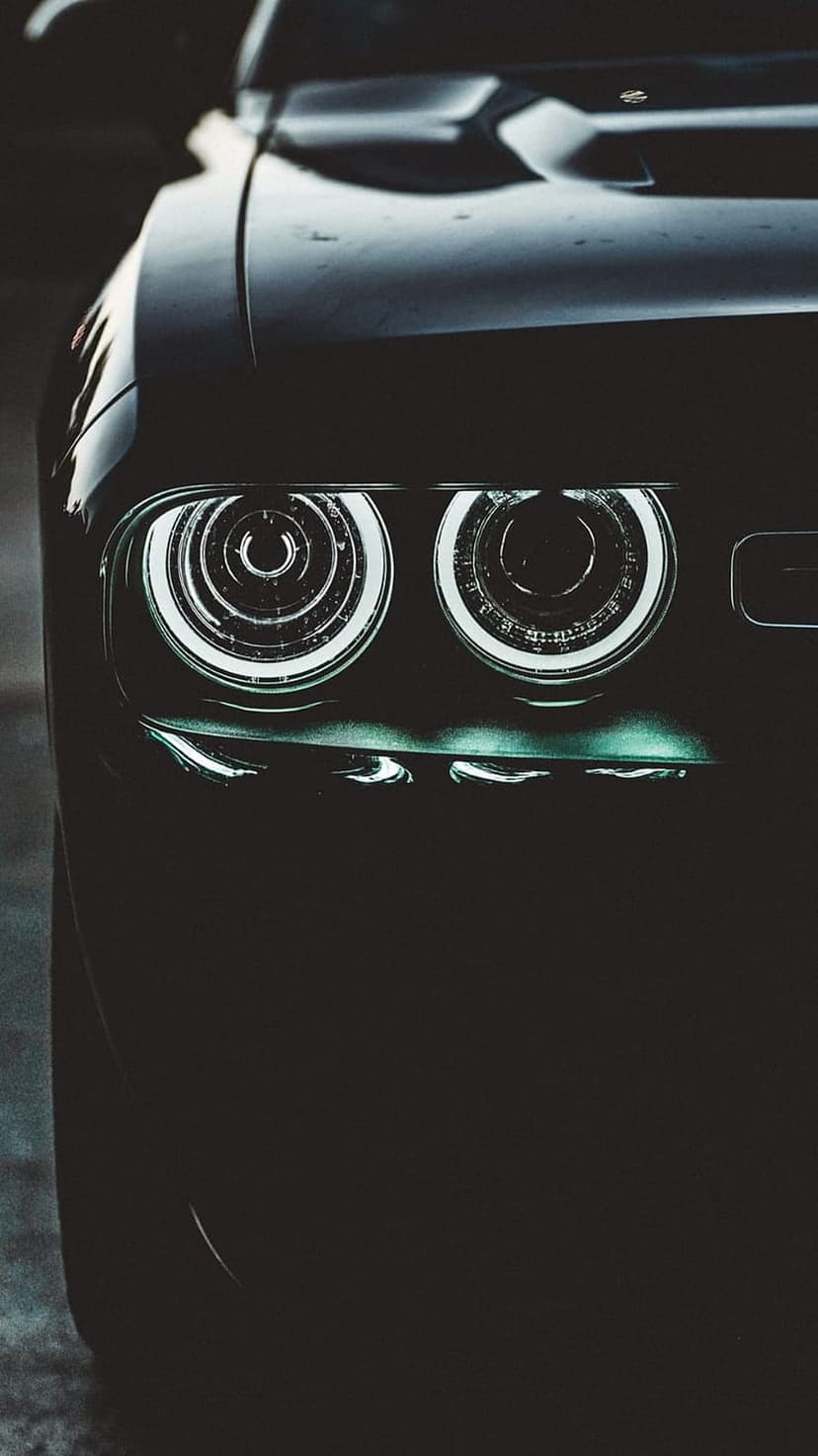Dodge Challenger circular LED headlights glowing with teal and white light against a dark front grille at night.