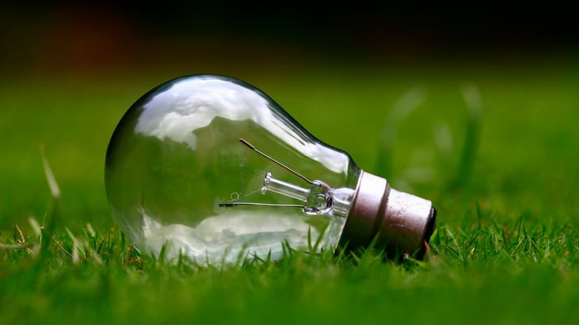 Clear glass bulb nestled in green grass reflecting a bright sky with clouds in a vertical macro perspective.