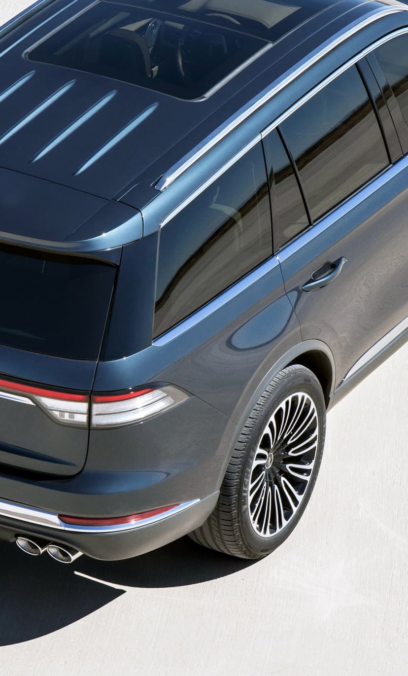 Rear view of a dark blue luxury SUV with a panoramic sunroof and chrome trim on a light concrete surface.