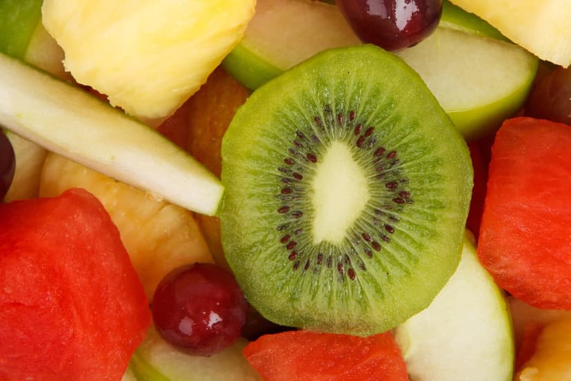 Sliced green kiwi with black seeds sits among red watermelon cubes and purple grapes in a macro fruit bowl.