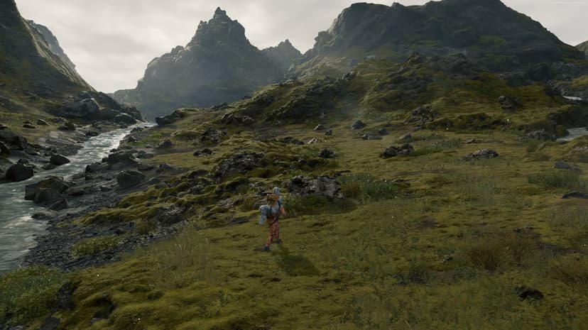 Man in cargo suit walking through a green mossy valley with a river and jagged mountains under cloudy skies.