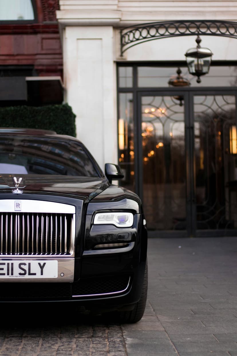 Rolls-Royce Ghost parked at a grand hotel entrance with glowing lanterns and a chrome Spirit of Ecstasy mascot.