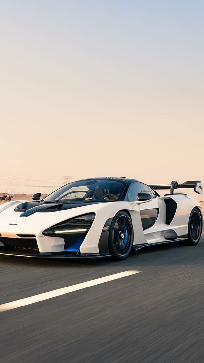White McLaren Senna hypercar driving on a desert road under a soft orange sunset sky at a low angle.