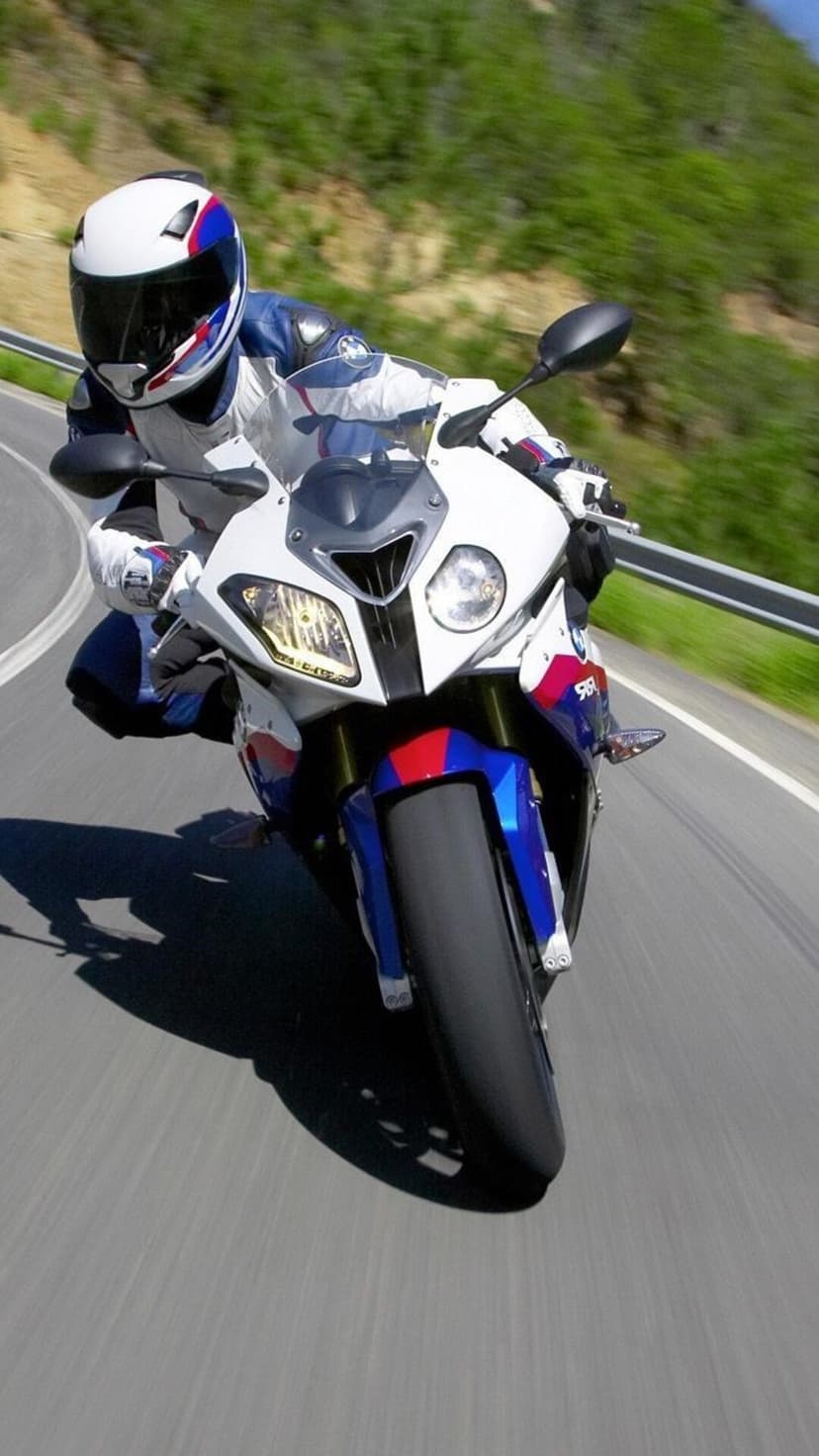 Motorcyclist in blue and white racing gear leans a sportbike into a sharp curve on a scenic mountain road.