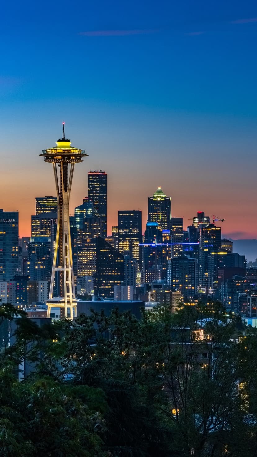 Space Needle rises above the glowing Seattle skyline under a blue and orange twilight sky in a vertical view.
