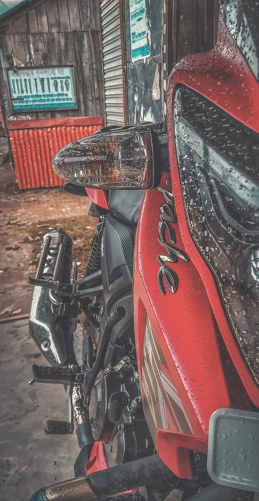 Red motorcycle fairing with translucent water droplets, chrome hardware, and a rustic wooden background.