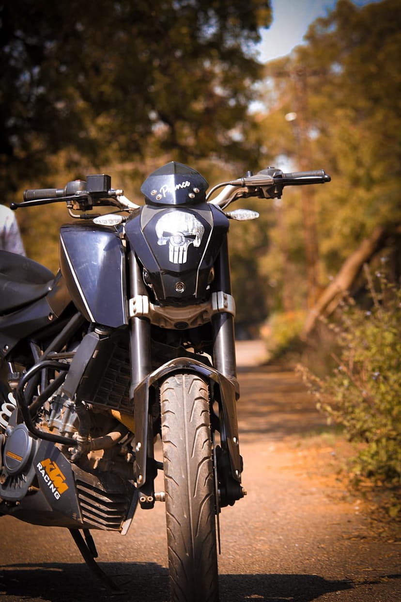Black KTM Duke motorcycle with a Punisher skull decal on the front fairing parked on a sunlit dirt road.