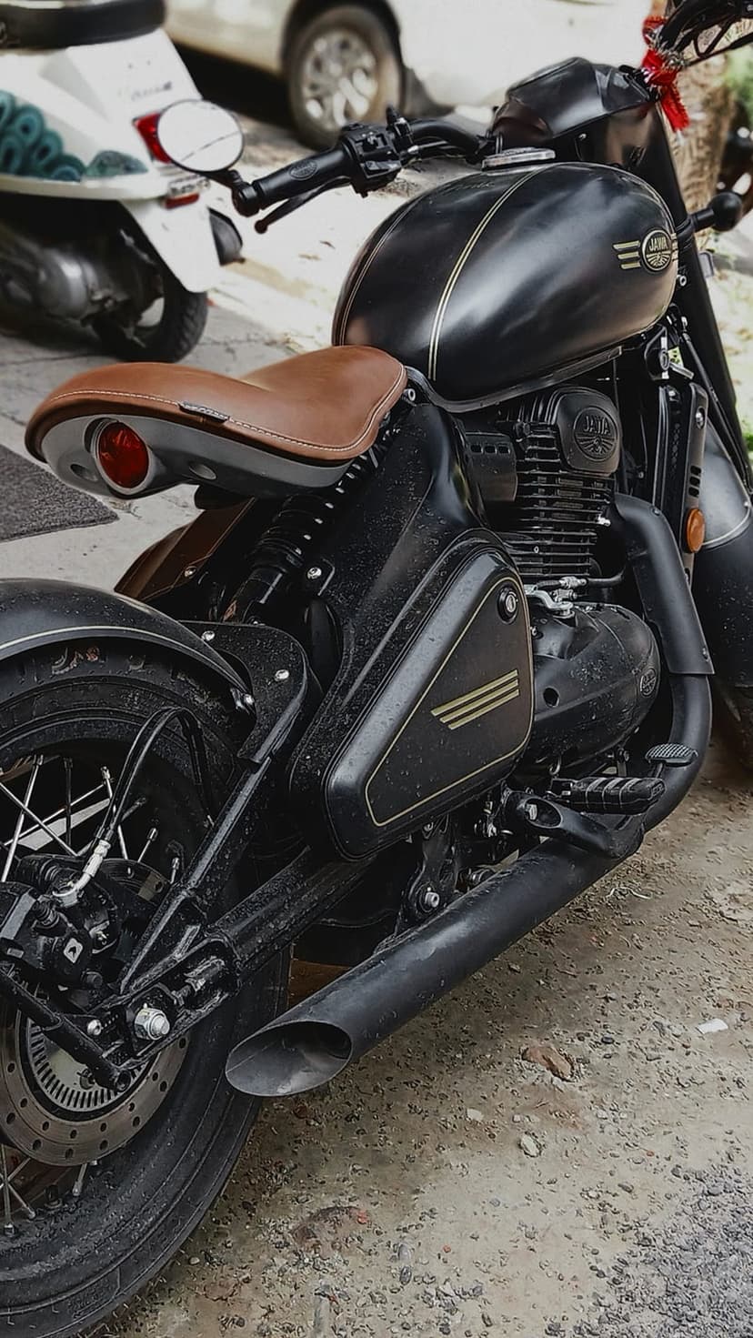 Black Jawa motorcycle featuring a brown leather seat, chrome exhaust pipe, and metallic engine parts outdoors.