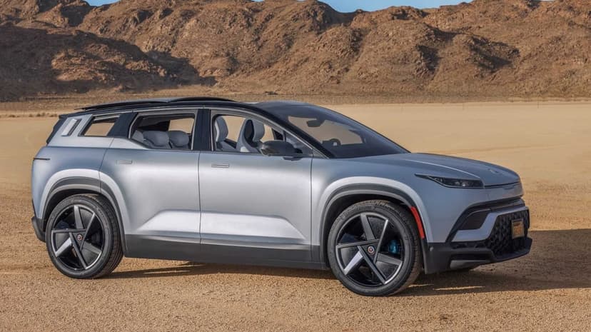 Silver electric SUV side profile parked on a sandy desert flat with rugged mountains under a clear sky.