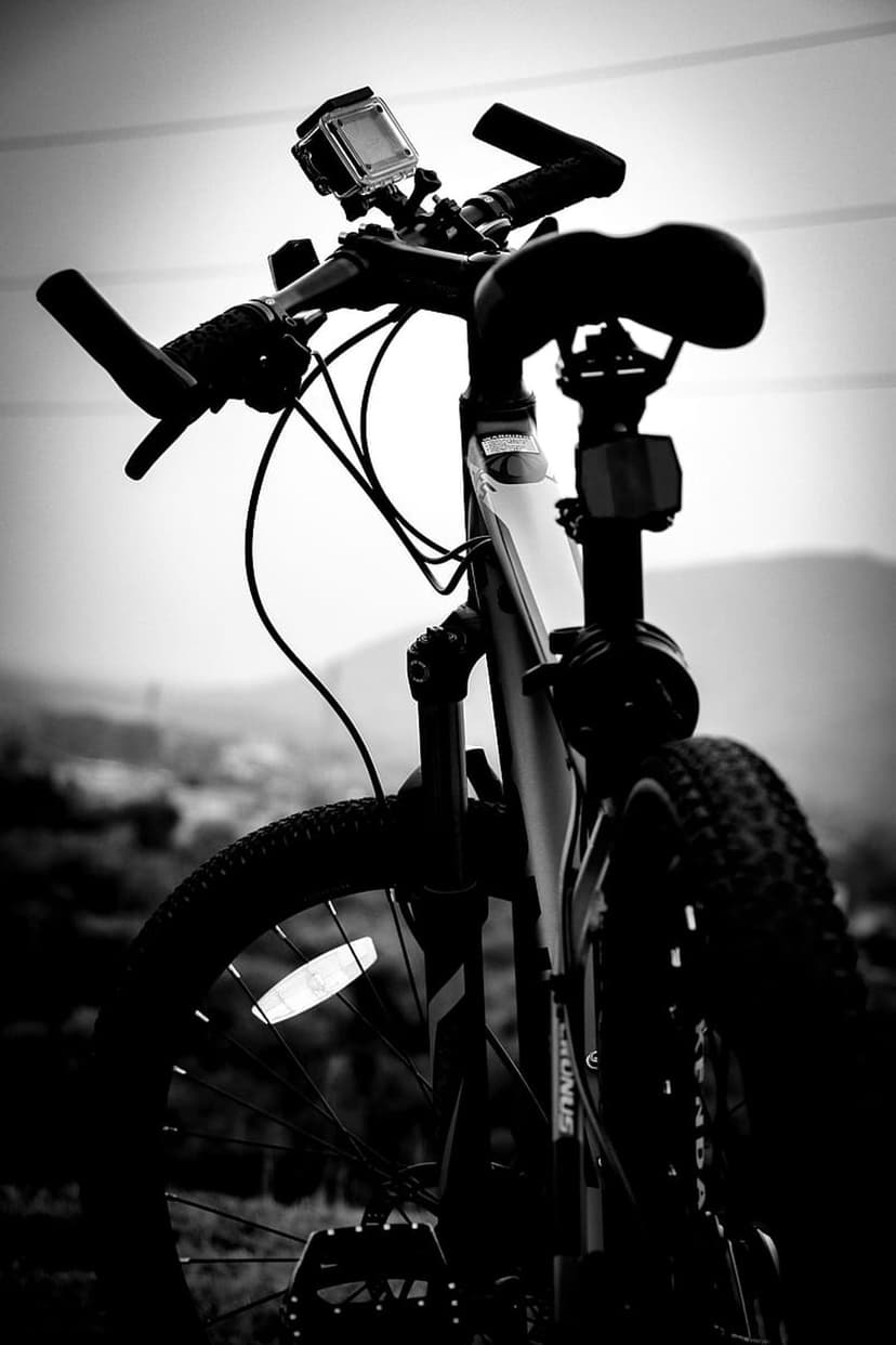 Mountain bike handlebars with a mounted action camera and front tire against a blurred hilly landscape.