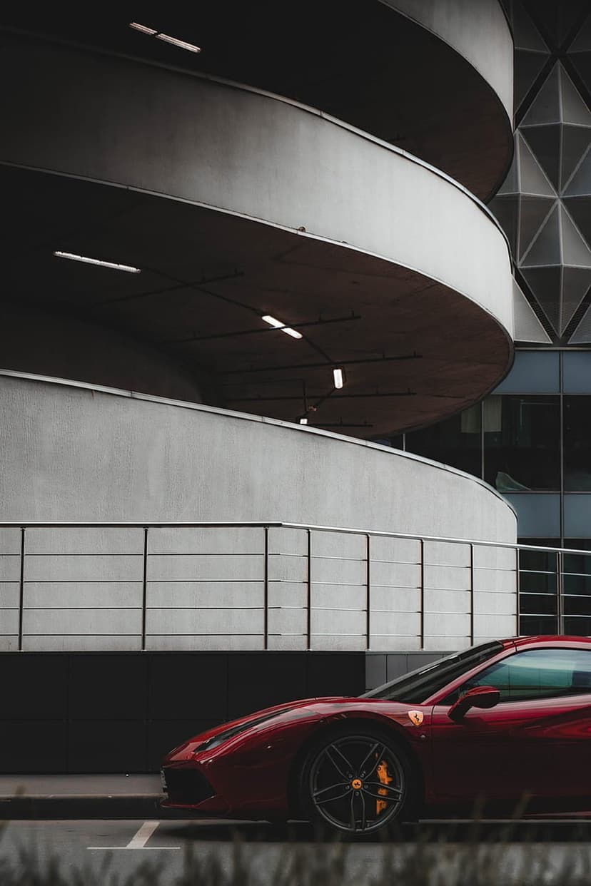 Red Ferrari sports car parked on a concrete ramp in front of a minimalist building with a geometric facade.