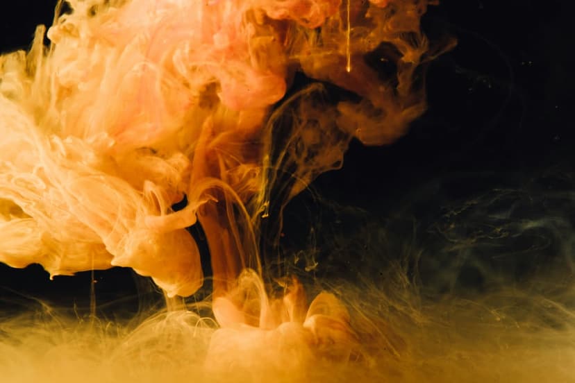Bright orange ink plumes bloom and swirl through deep black water in a high-contrast display of fluid motion.