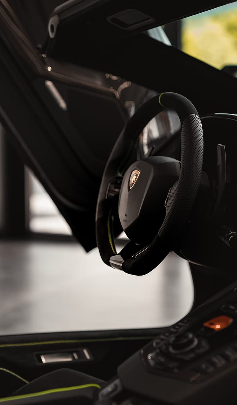 Steering wheel with lime green stitching and perforated leather in a luxury car interior with carbon fiber trim.