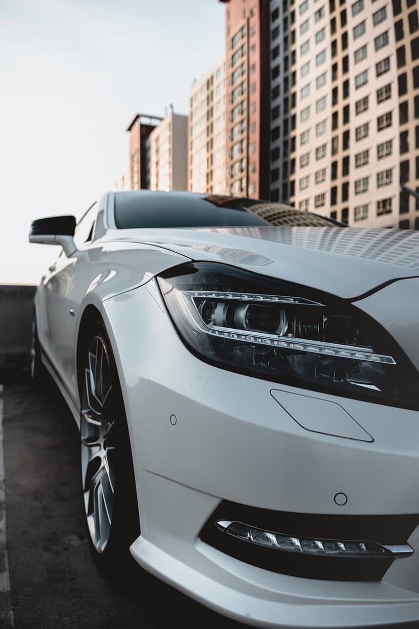 White luxury car parked on an urban street with modern glass buildings reflecting bright daylight in the city.