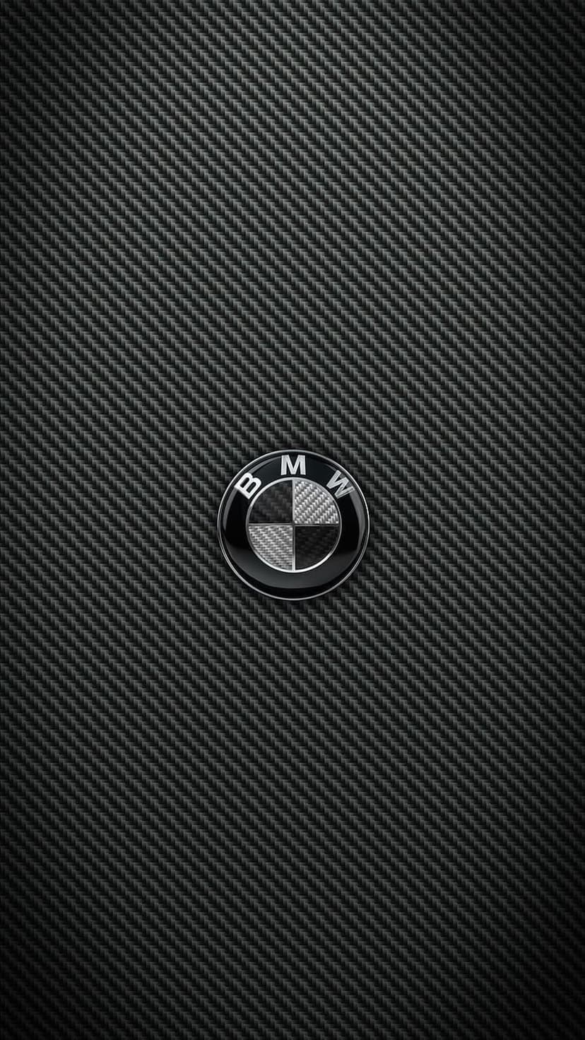 BMW emblem centered on a dark matte carbon fiber background with realistic woven textures and metallic reflections.