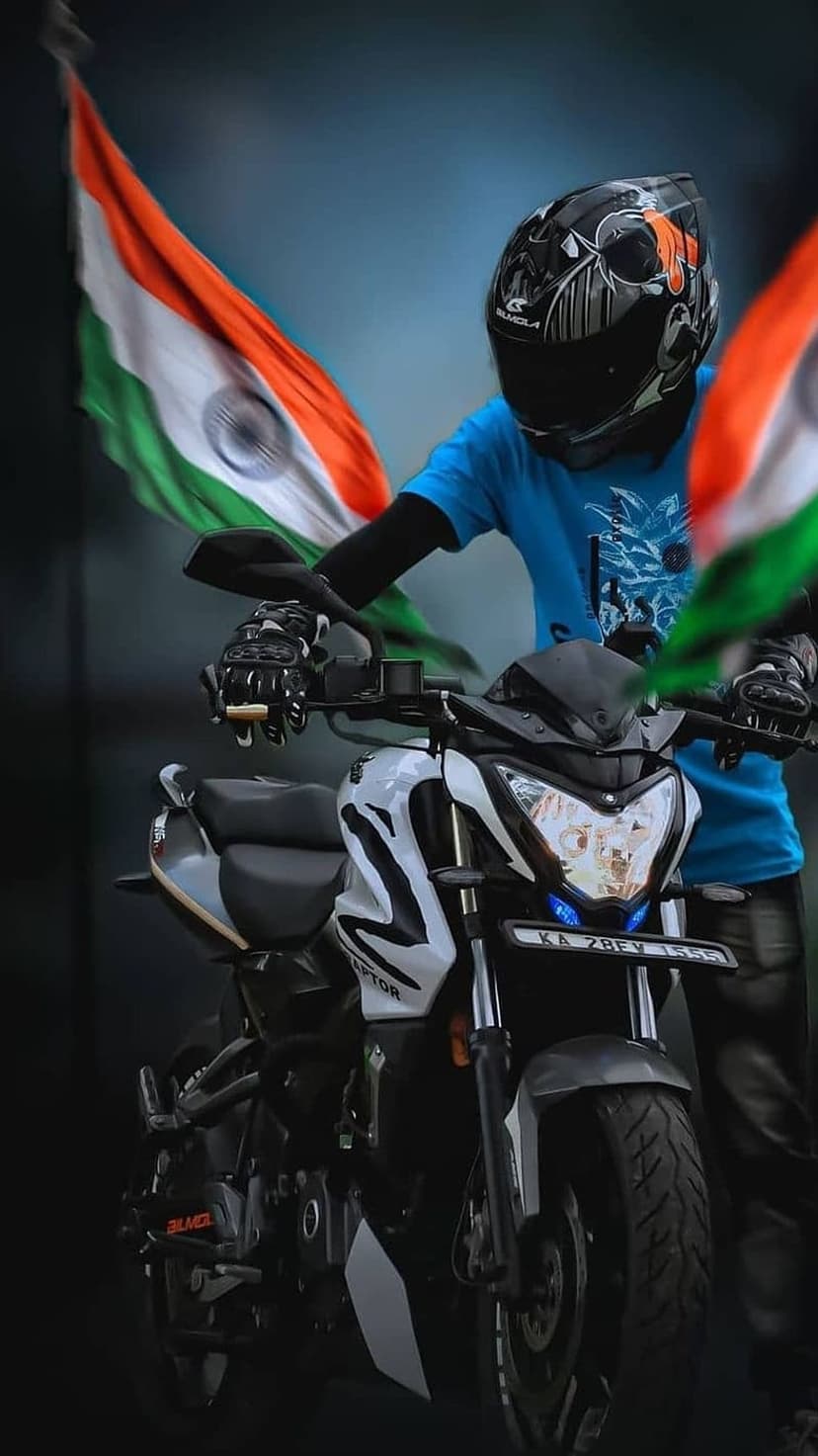 Indian man in a blue shirt and helmet stands next to a white motorcycle decorated with the national tricolor flag.