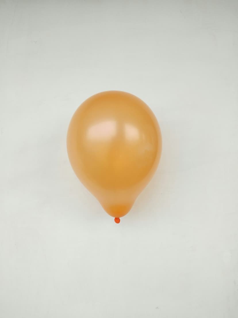 Orange balloon with a small red knot sits centered on a white textured background in an overhead studio view.