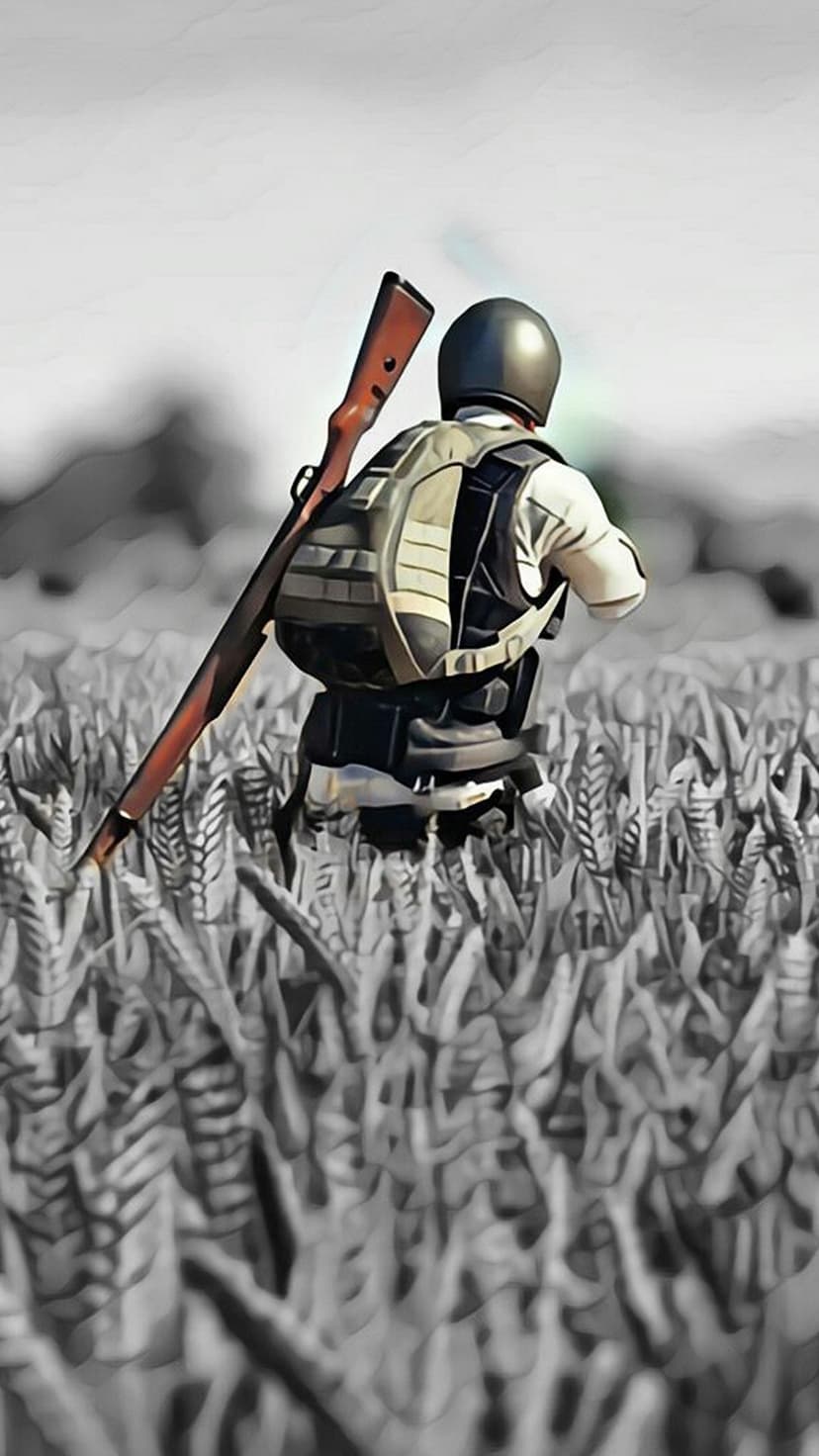 Tactical soldier in full combat gear crouches among tall wheat stalks with a long rifle slung across their back.