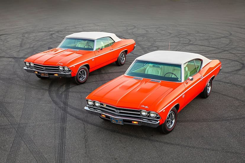 Two bright orange classic Chevrolet Chevelle SS cars with white tops on an asphalt surface with tire marks.