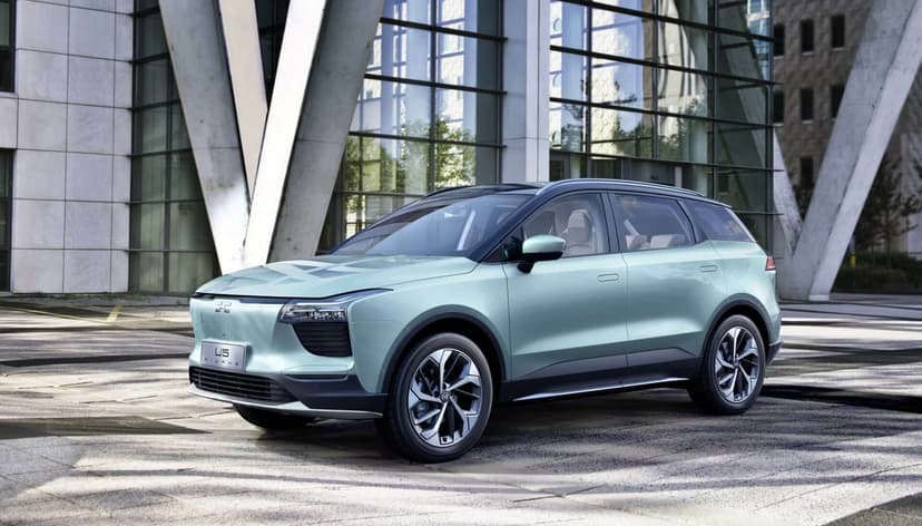 Mint green electric SUV parked in front of a modern glass building with concrete pillars in bright daylight.