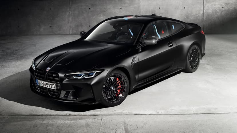 Matte black BMW M4 sports car with red brake calipers parked inside a dark, industrial concrete studio setting.