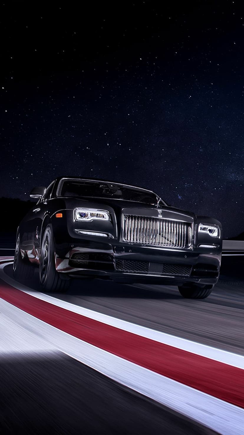 Black Rolls-Royce Wraith driving on a curved track under a starry night sky with glowing headlights.