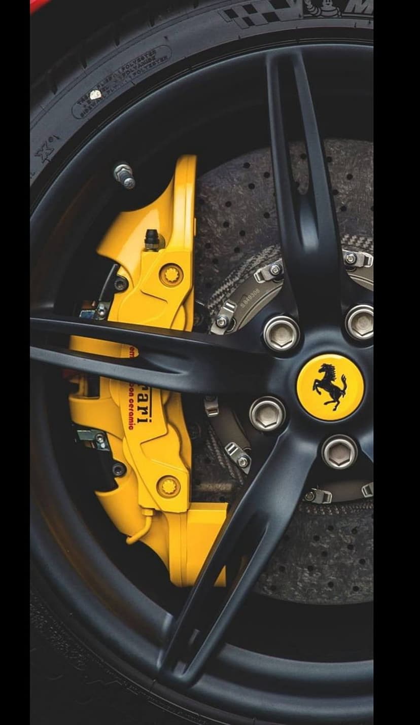 Yellow Ferrari brake caliper with carbon ceramic text sits behind a matte black multi-spoke alloy rim and emblem.
