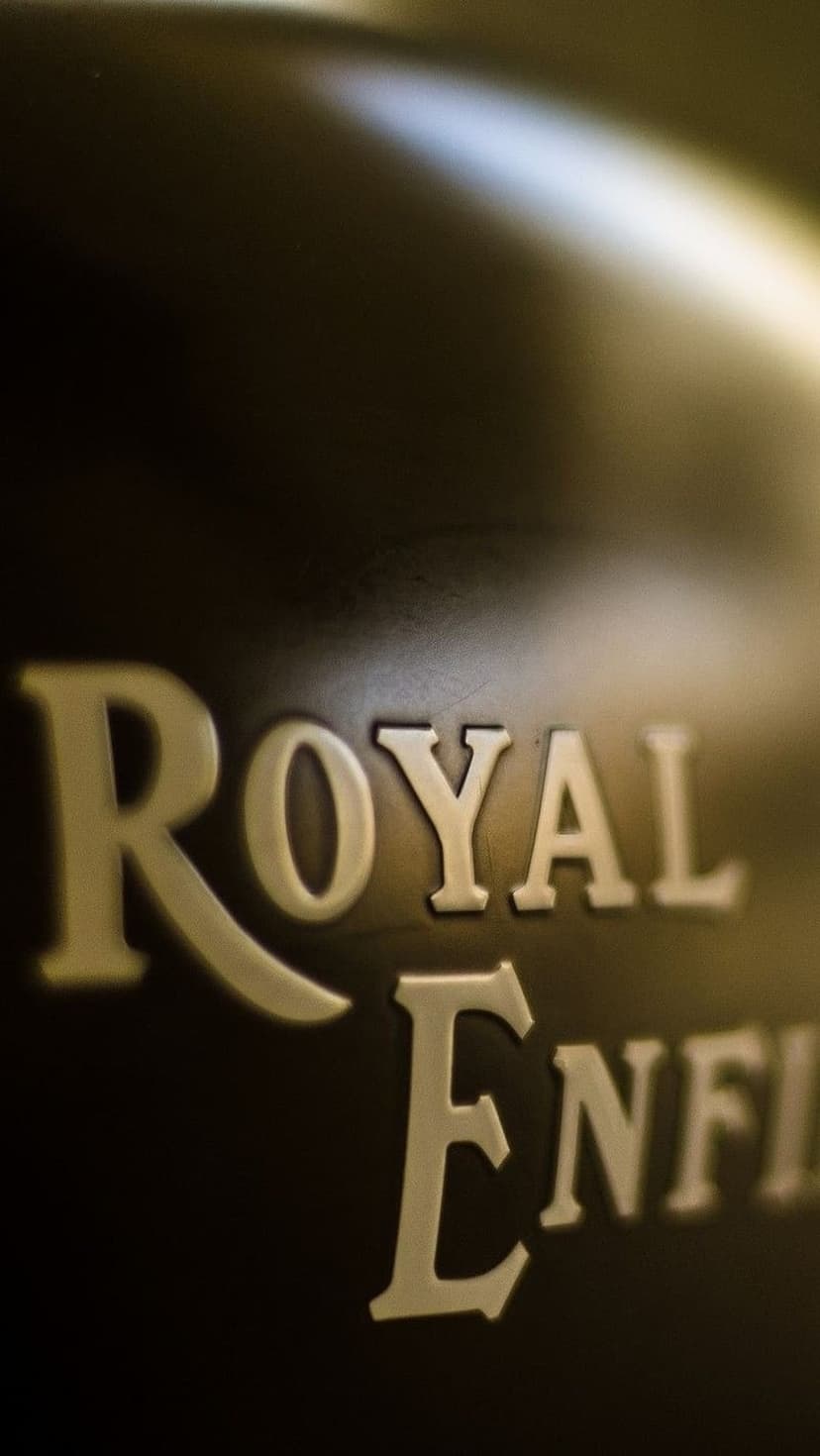 Royal Enfield metallic emblem with embossed lettering glinting on a dark textured background in close-up detail.